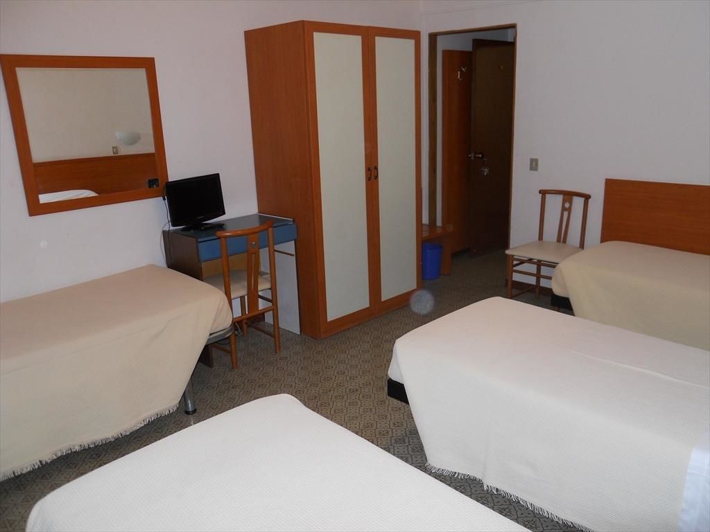 Une chambre d’hôtel avec deux lits, un bureau avec un ordinateur, une armoire et un miroir.