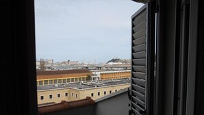 Vista desde un balcón con un paisaje urbano de fondo, que incluye edificios y un puente.