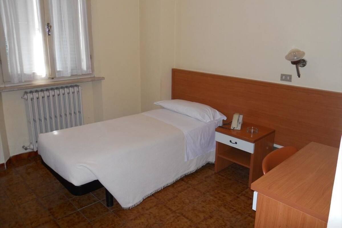 A single bed with a wooden headboard, a bedside table with a lamp, and a small desk with a chair.