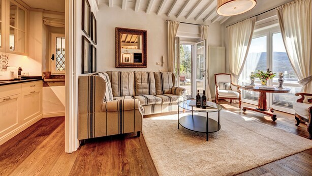 A spacious living room with a sofa, a coffee table, and a dining area with a table and chairs. There is a large window providing natural light and a view of the outdoors. - Terre di Baccio (Greve in Chianti)