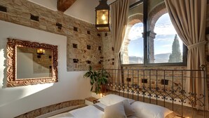 A bedroom with a stone wall, a large mirror, a bed with white linens, a potted plant, and a view through a window with curtains. - Terre di Baccio (Greve in Chianti)