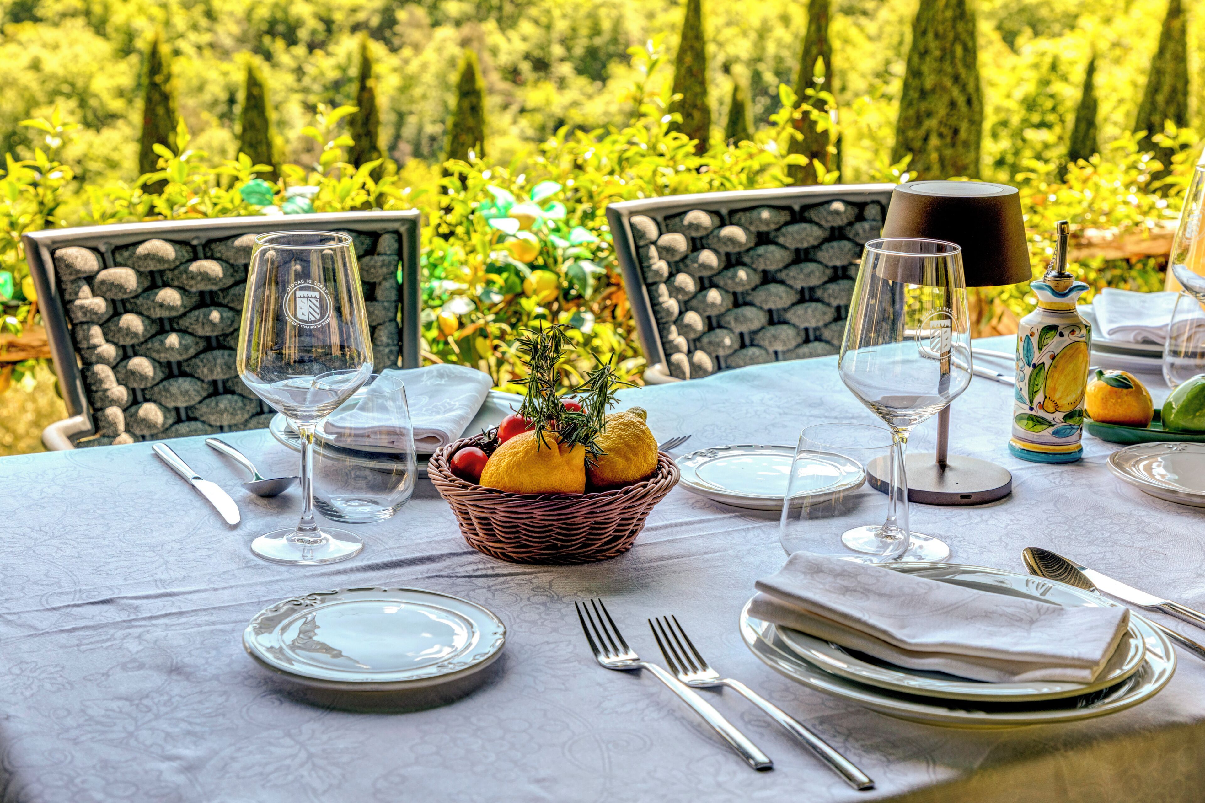 Une table dressée pour le repas, avec un panier de fruits, des verres à vin et des couverts.