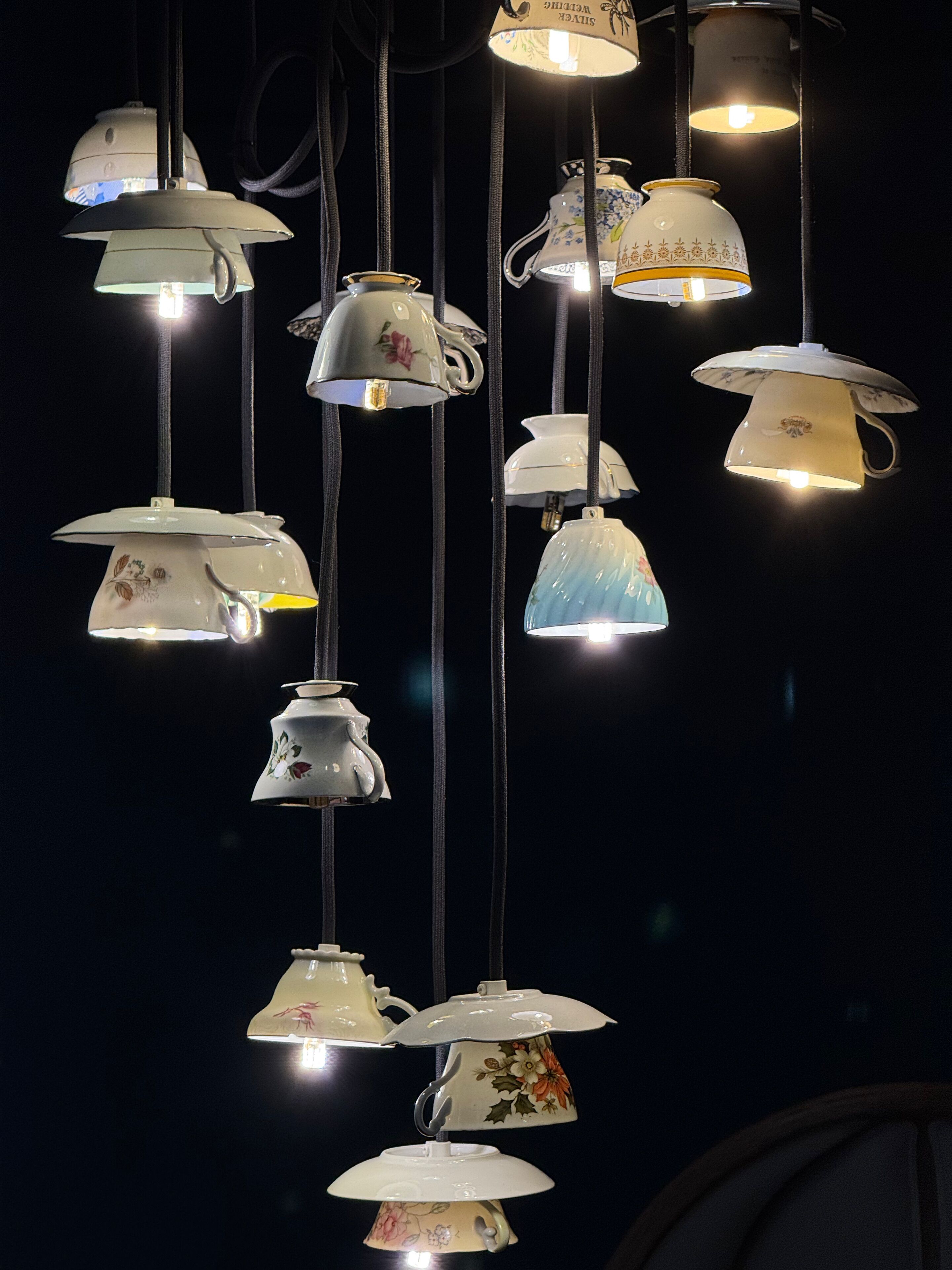 A collection of hanging light fixtures in the shape of teapots and cups, each with a lit bulb.