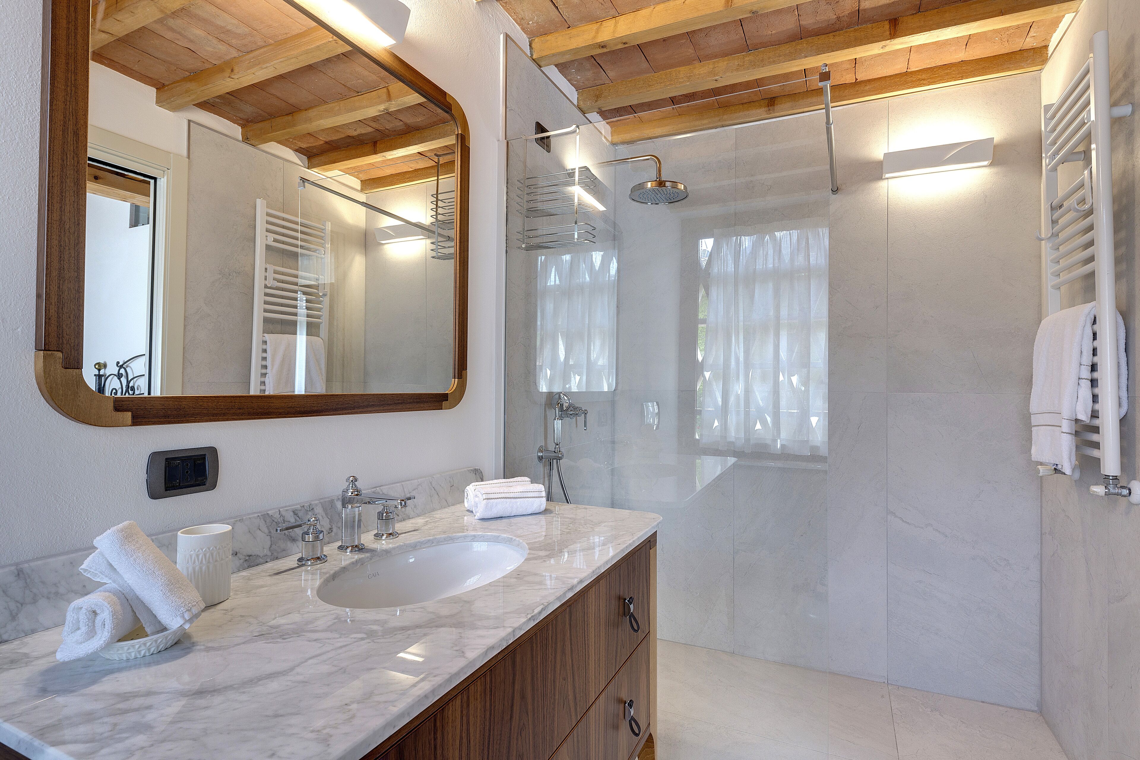 A modern bathroom with a large mirror, marble sink, wooden cabinets, and a glass-enclosed shower.