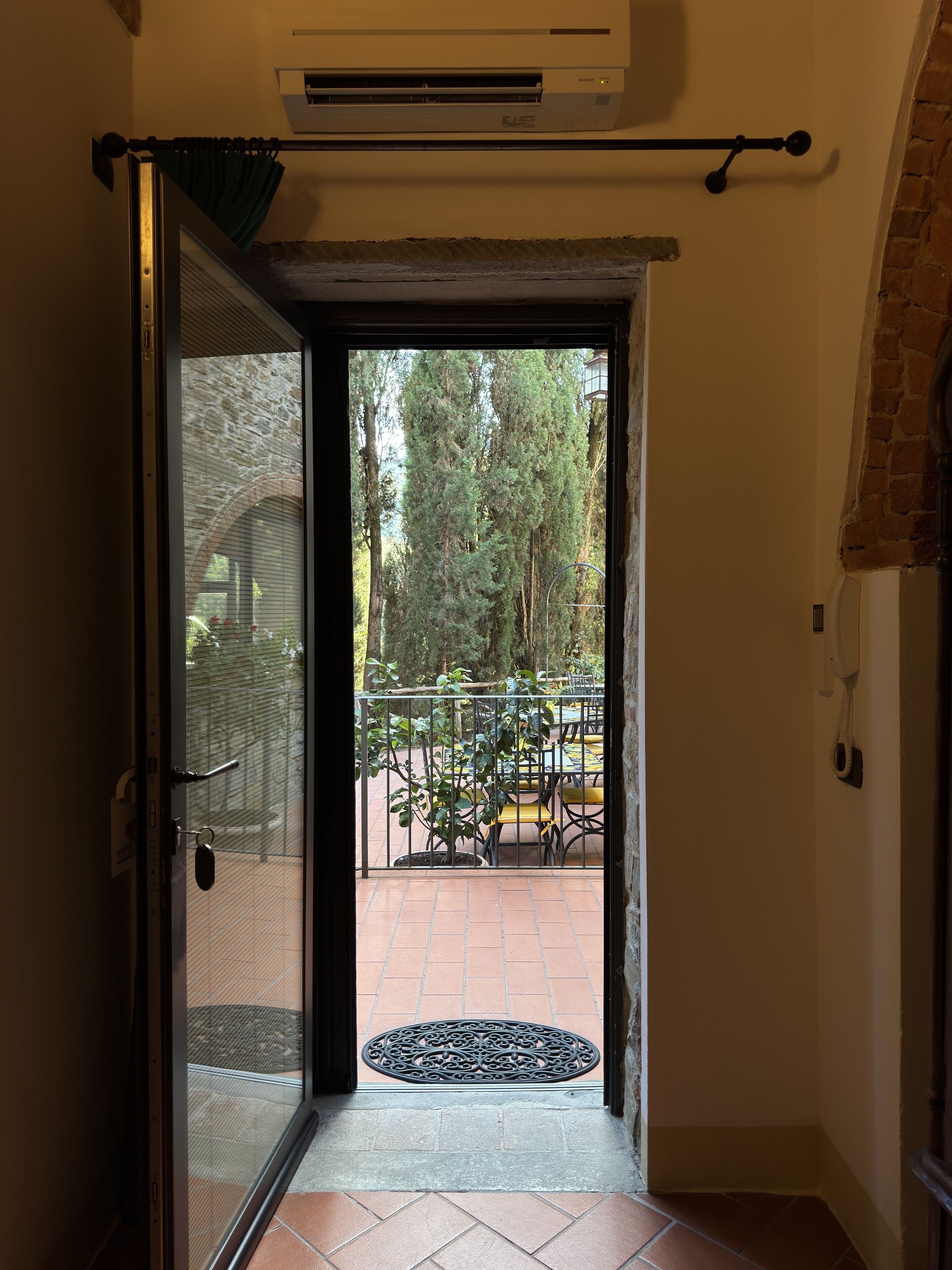 Une porte donnant sur un patio avec vue sur des arbres et un mur de briques.