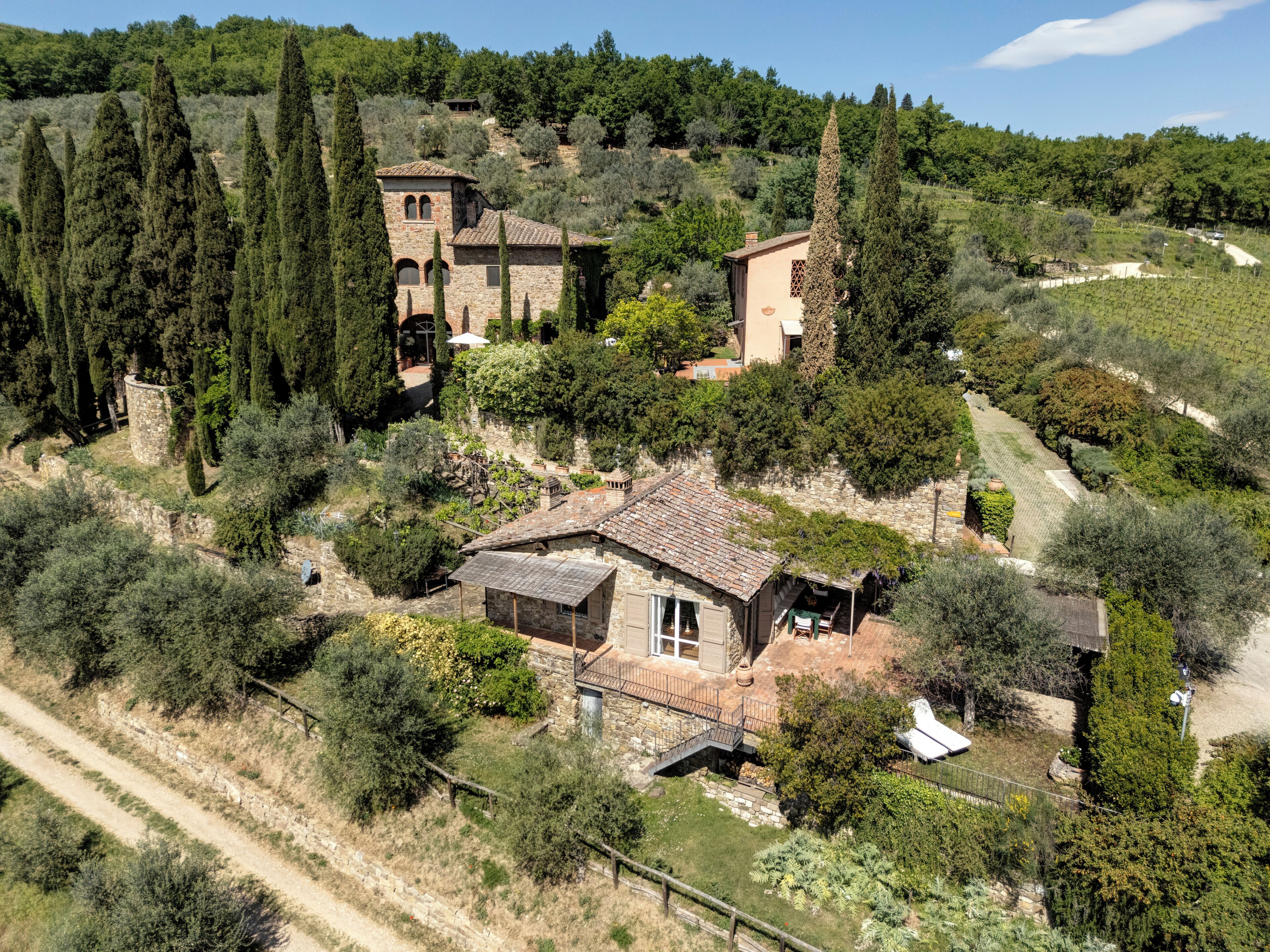 Una villa de piedra con techo de tejas, rodeada de olivares y altos cipreses.