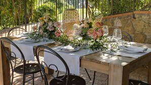 An outdoor dining area with a stone wall backdrop, metal chairs, and a table set with white tablecloths, plates, and glassware. - Terre di Baccio (Greve in Chianti)