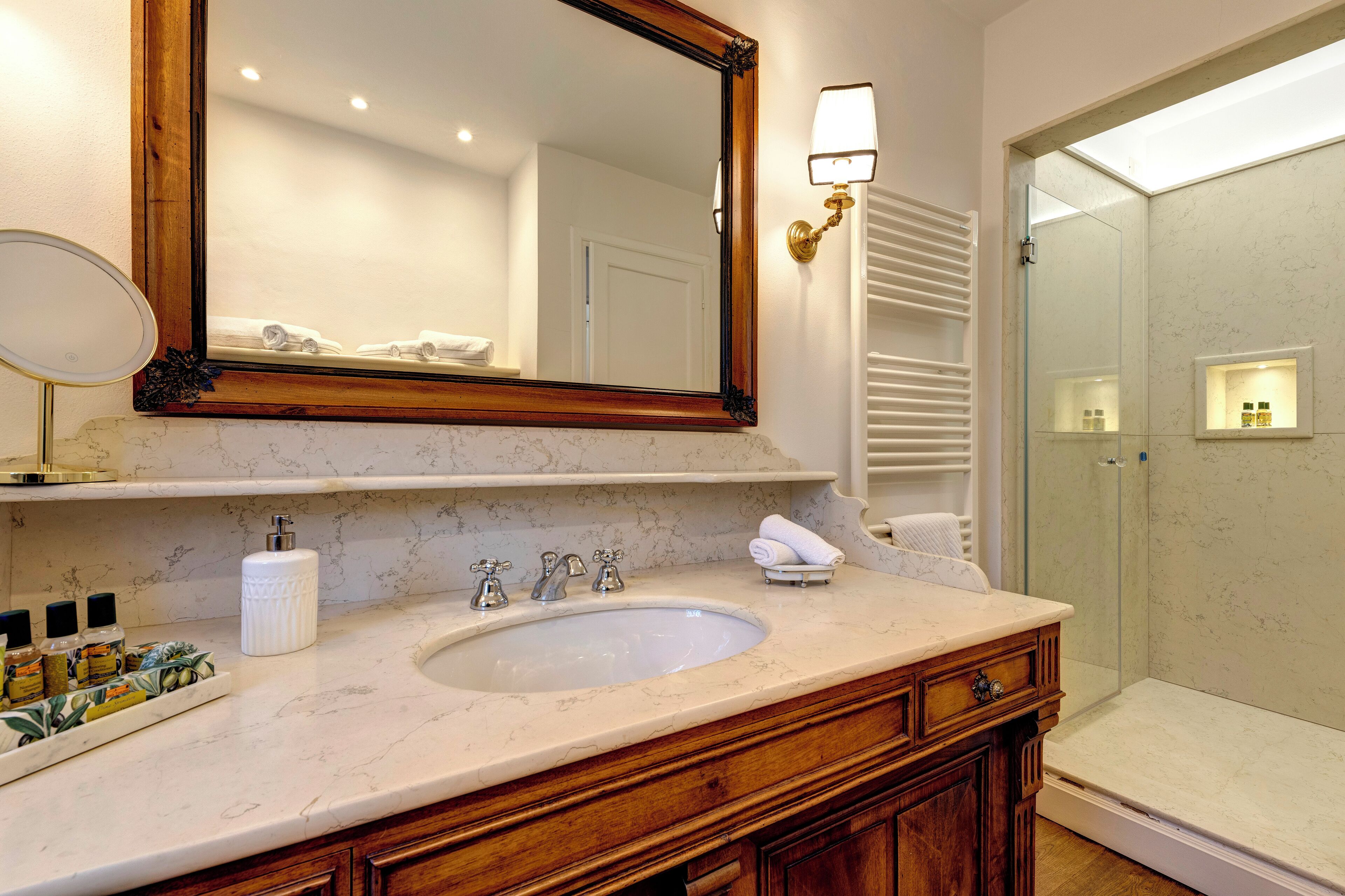 Une salle de bain avec un lavabo en marbre, un meuble-lavabo en bois, un grand miroir et une douche à parois de verre.