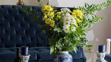 Ein Zimmer mit einem blauen Sofa, einem hölzernen Couchtisch mit dekorativen Vasen, einer Flasche und einem Teller mit Keksen.