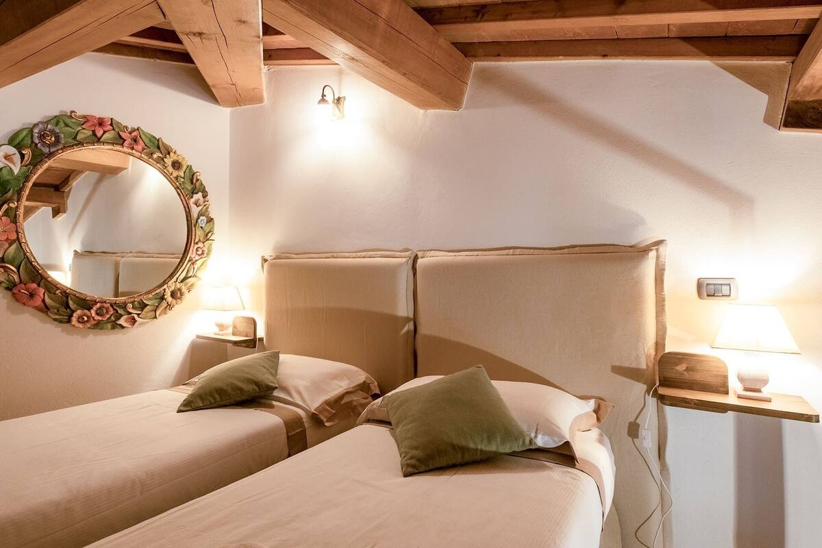 A bedroom with two beds, a wooden ceiling, a wall-mounted mirror, and bedside lamps.