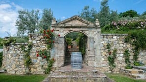 A stone archway with a barrel at its base, surrounded by greenery and flowering plants. - Terre di Baccio (Greve in Chianti)