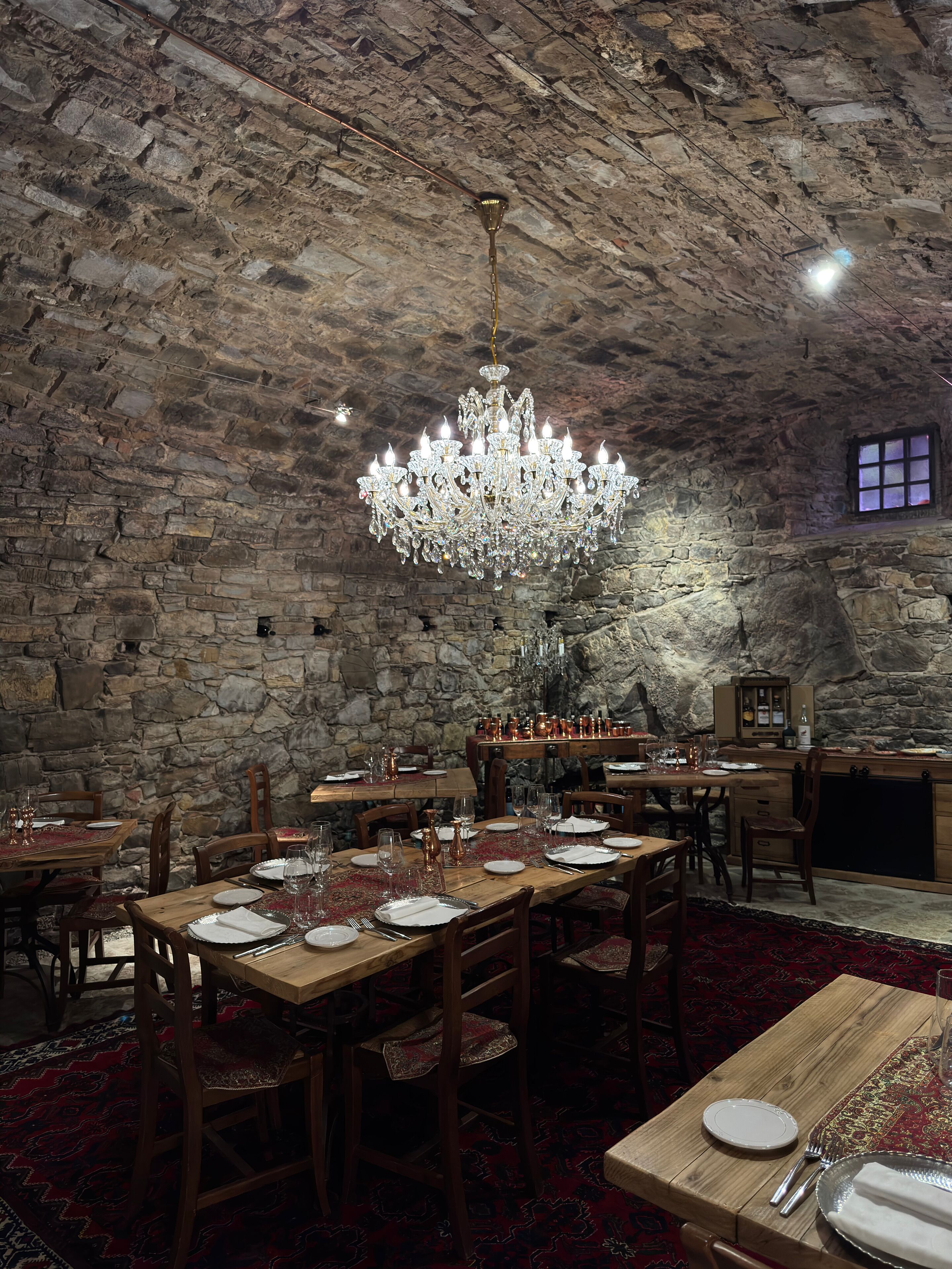 A restaurant with stone walls, wooden tables, and a chandelier.