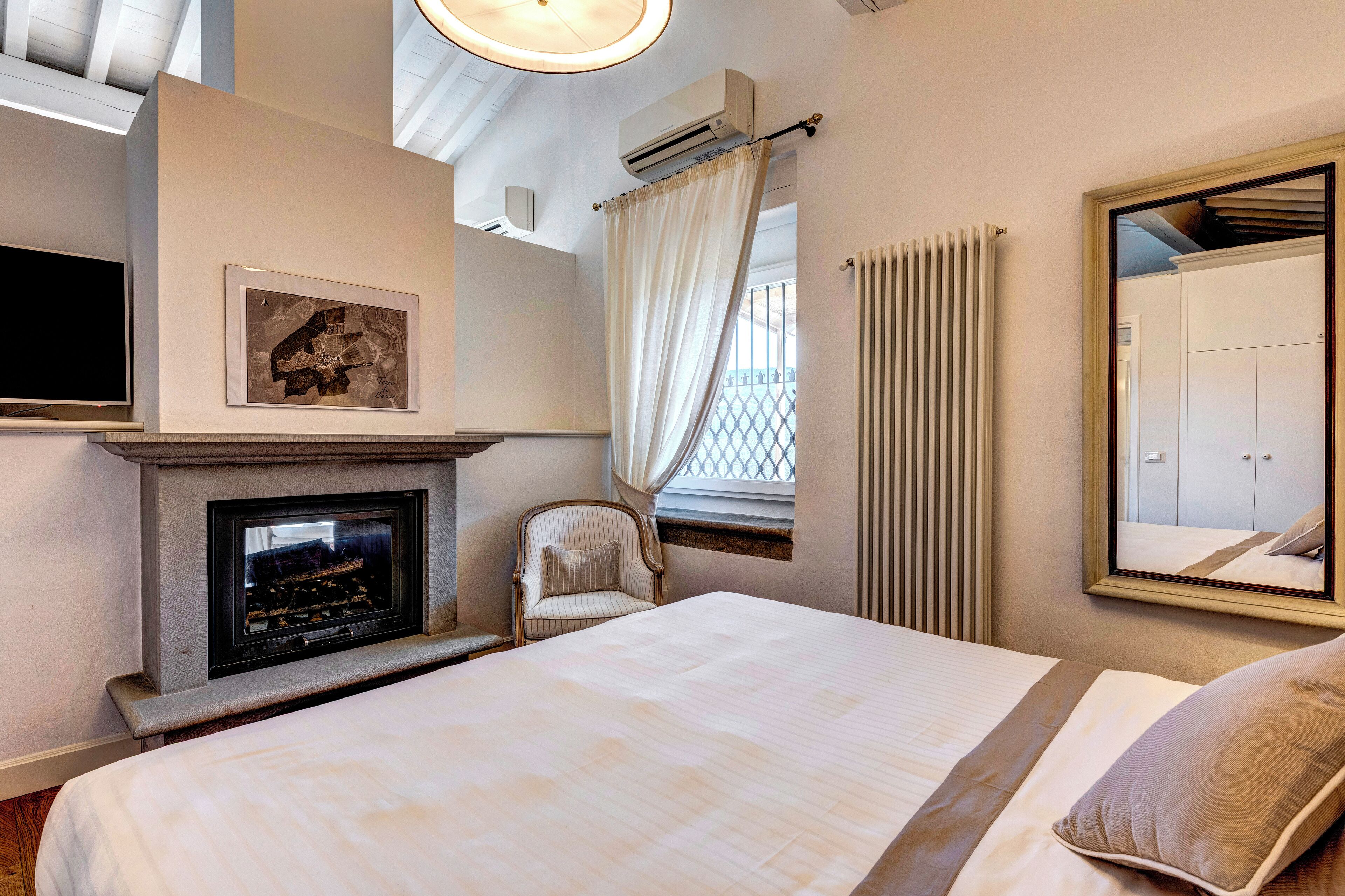 Habitación de hotel con cama, chimenea, una silla, espejo y ventana con cortinas.