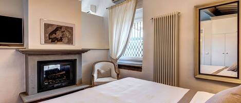 Habitación de hotel con cama, chimenea, una silla, espejo y ventana con cortinas.