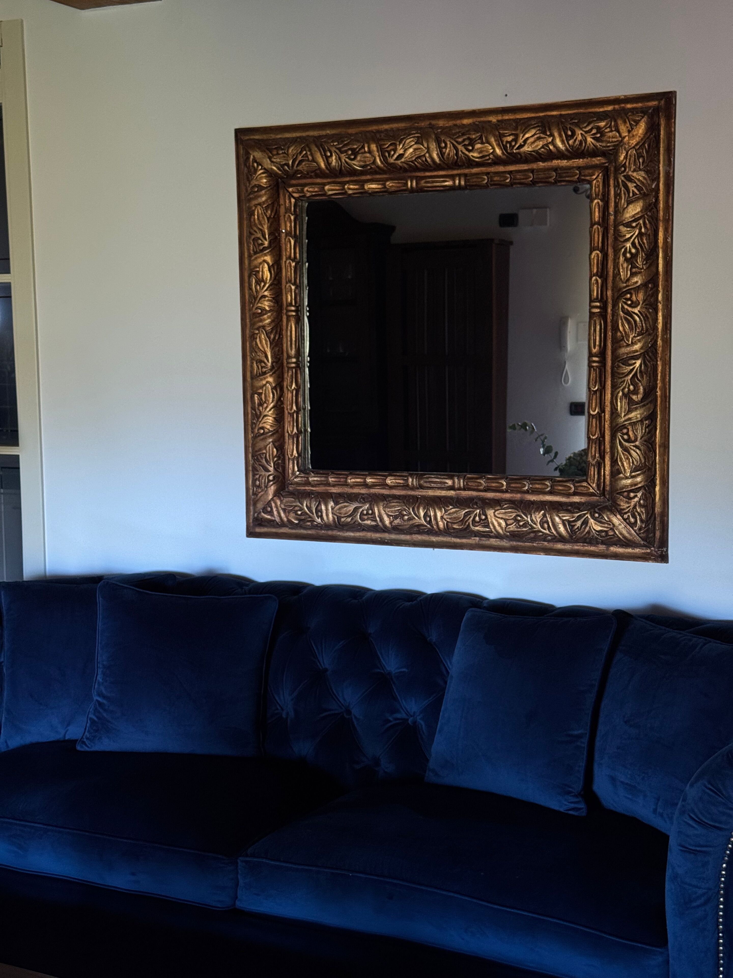 Ein dunkelblaues Sofa mit einem goldrahmigen Spiegel darüber.