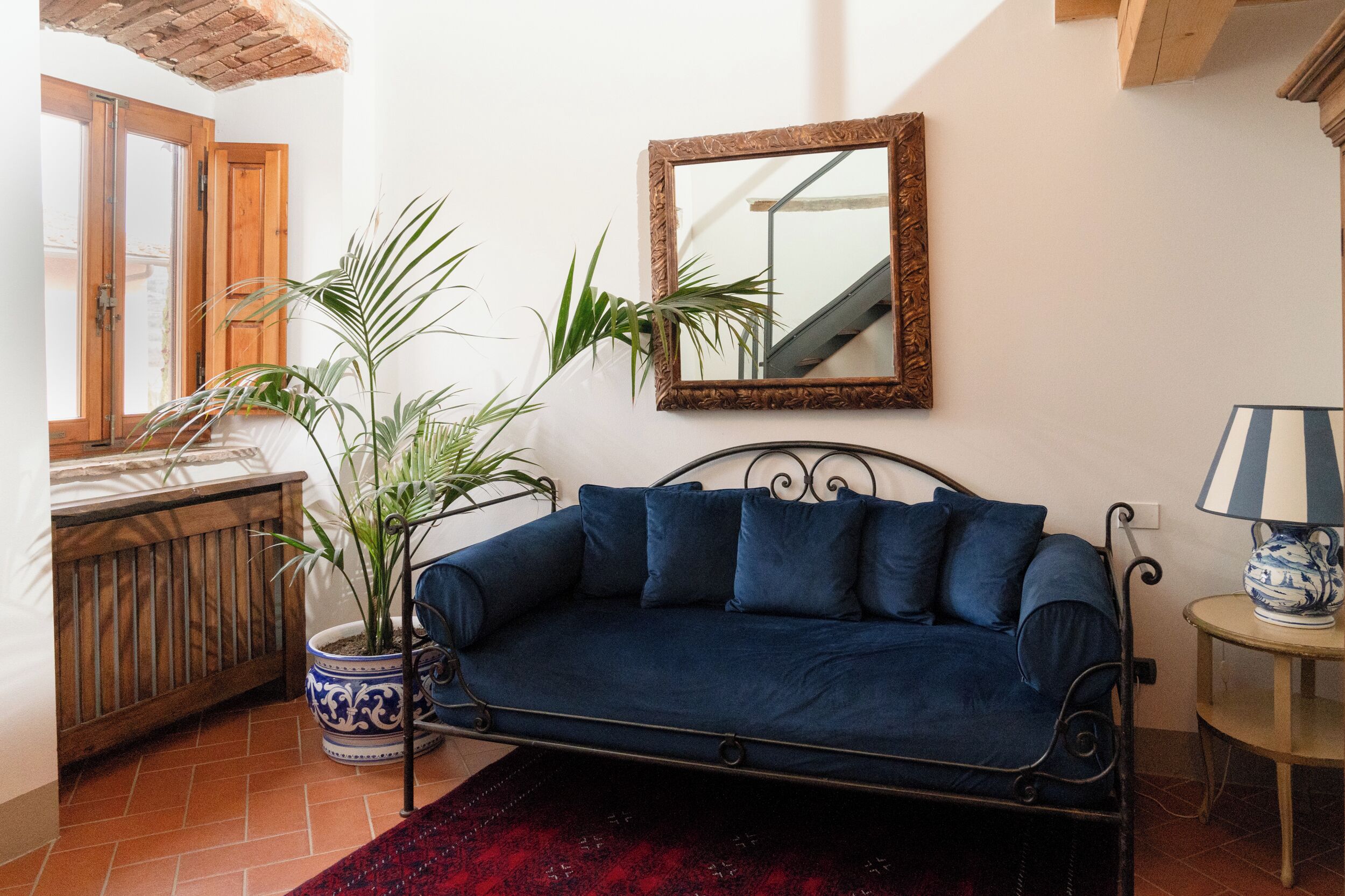 Une pièce avec un canapé bleu, une plante en pot, un miroir et une lampe.