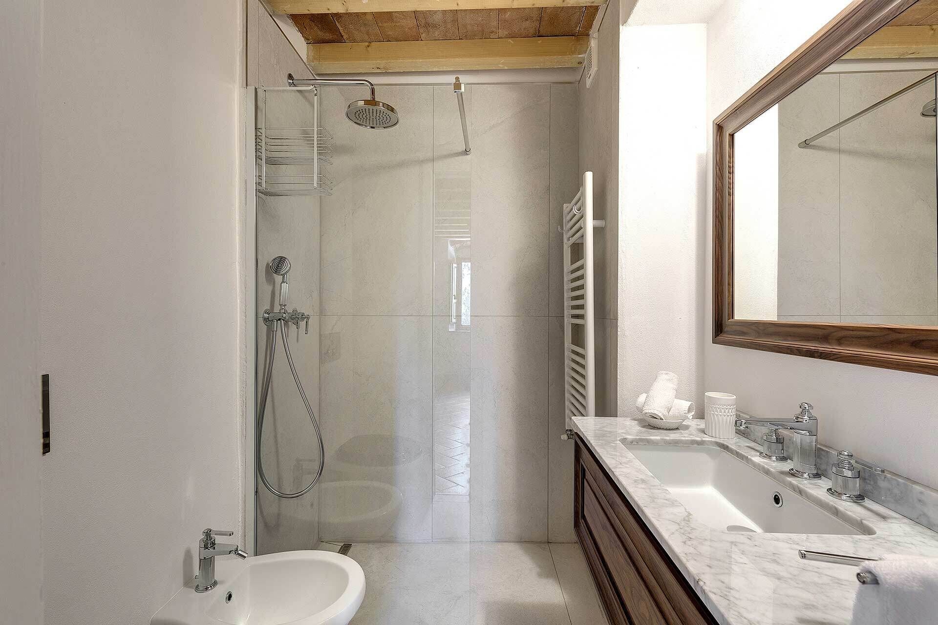 Et moderne badeværelse med en glasbrusekabine, et vaskeskab med håndvask og spejl, samt et toilet.