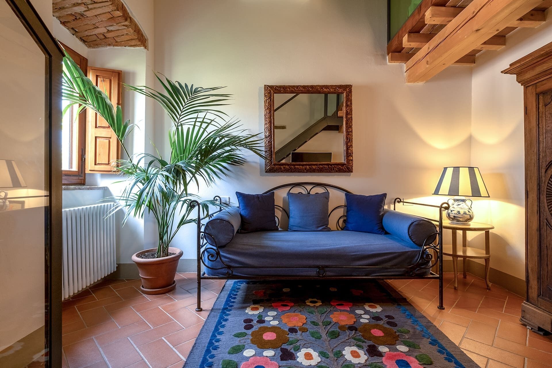 A cozy room with a bed, a potted plant, a mirror, and a lamp.