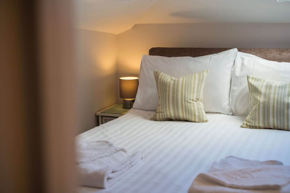 A neatly made bed with striped pillows, a bedside lamp, and a visible hand towel.