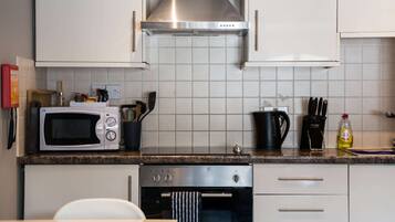 A kitchen with white cabinets, a stainless steel range hood, a microwave, and an oven.