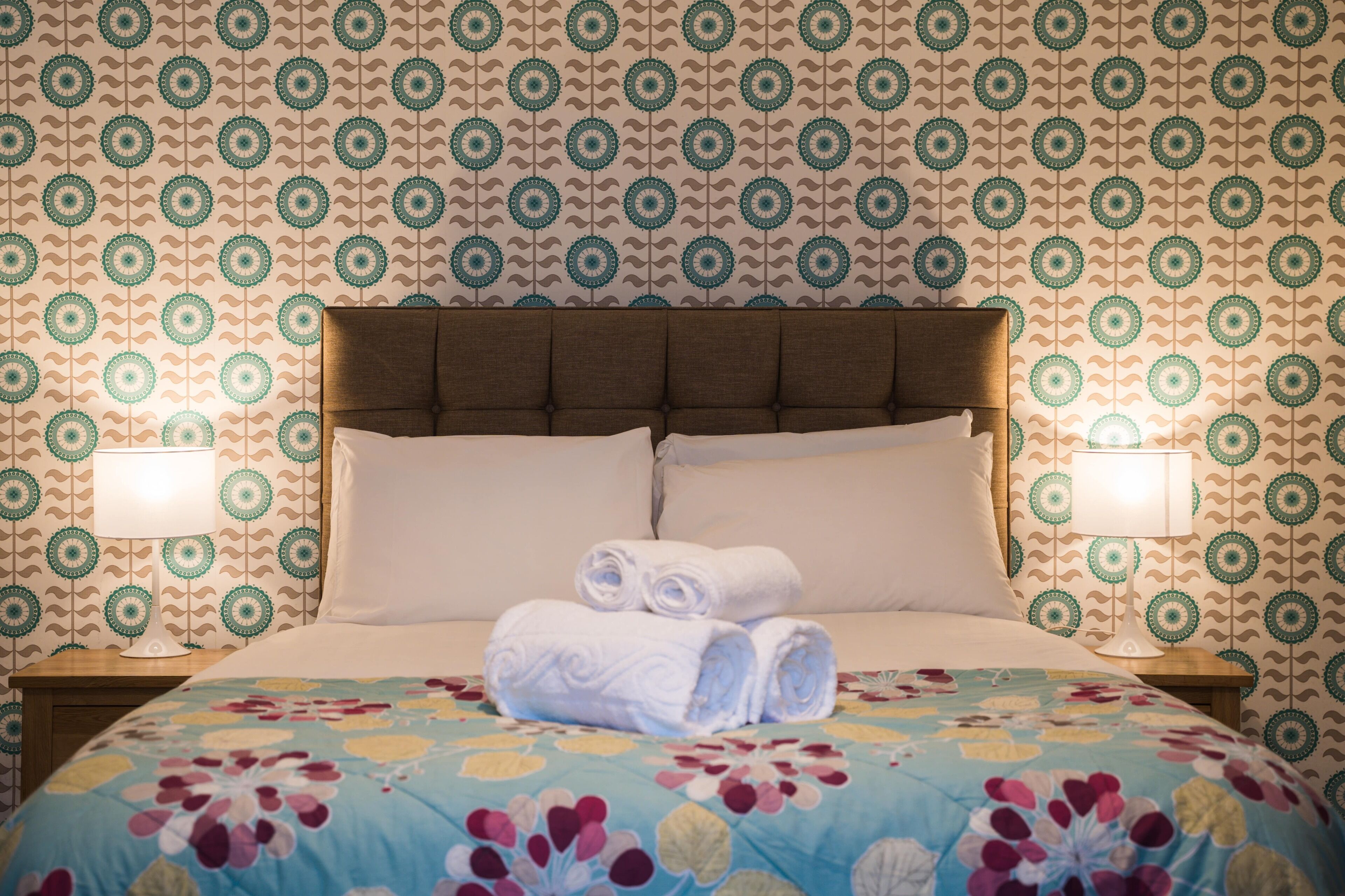 Una habitación de hotel con una cama grande, dos lámparas de noche y una colcha estampada con motivos florales.