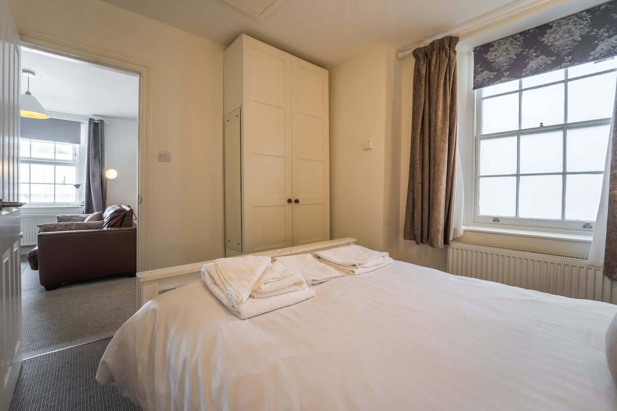 A hotel room with a bed, a wardrobe, a bathroom with a mirror, and a window with curtains.