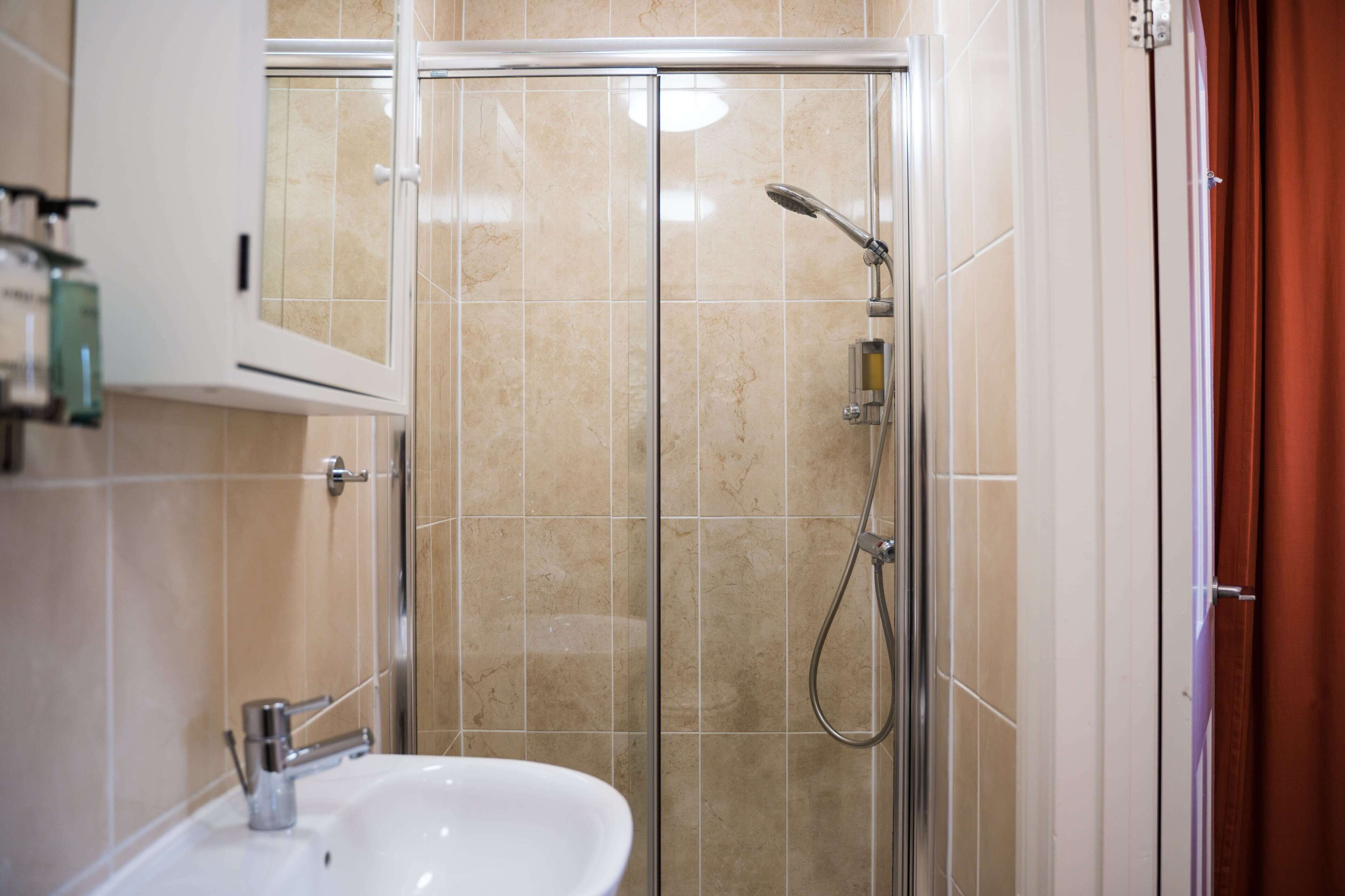 Een badkamer met douche, wastafel en kast.