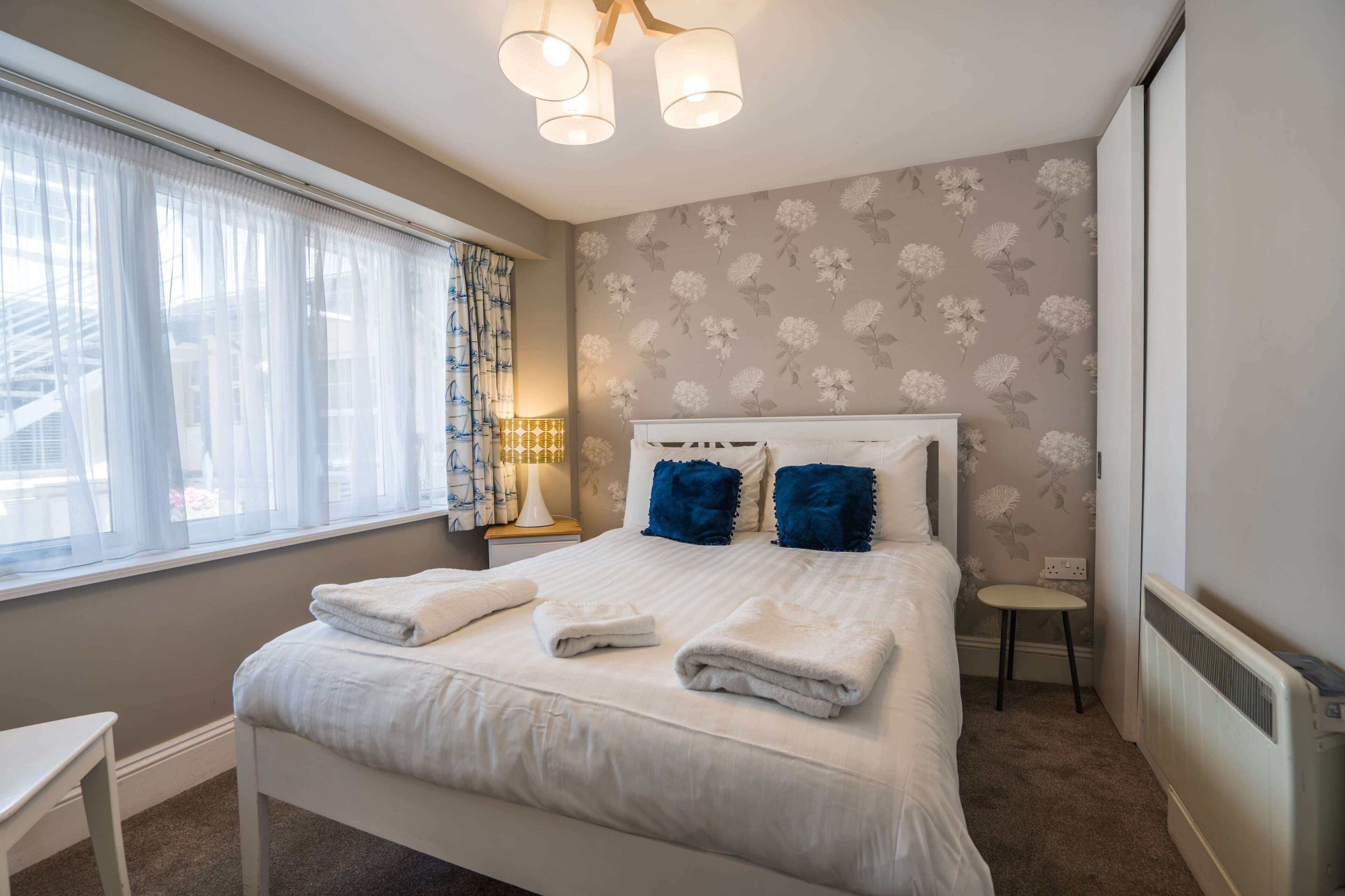 A neatly made bed with white and blue pillows, a bedside table, and a lamp.