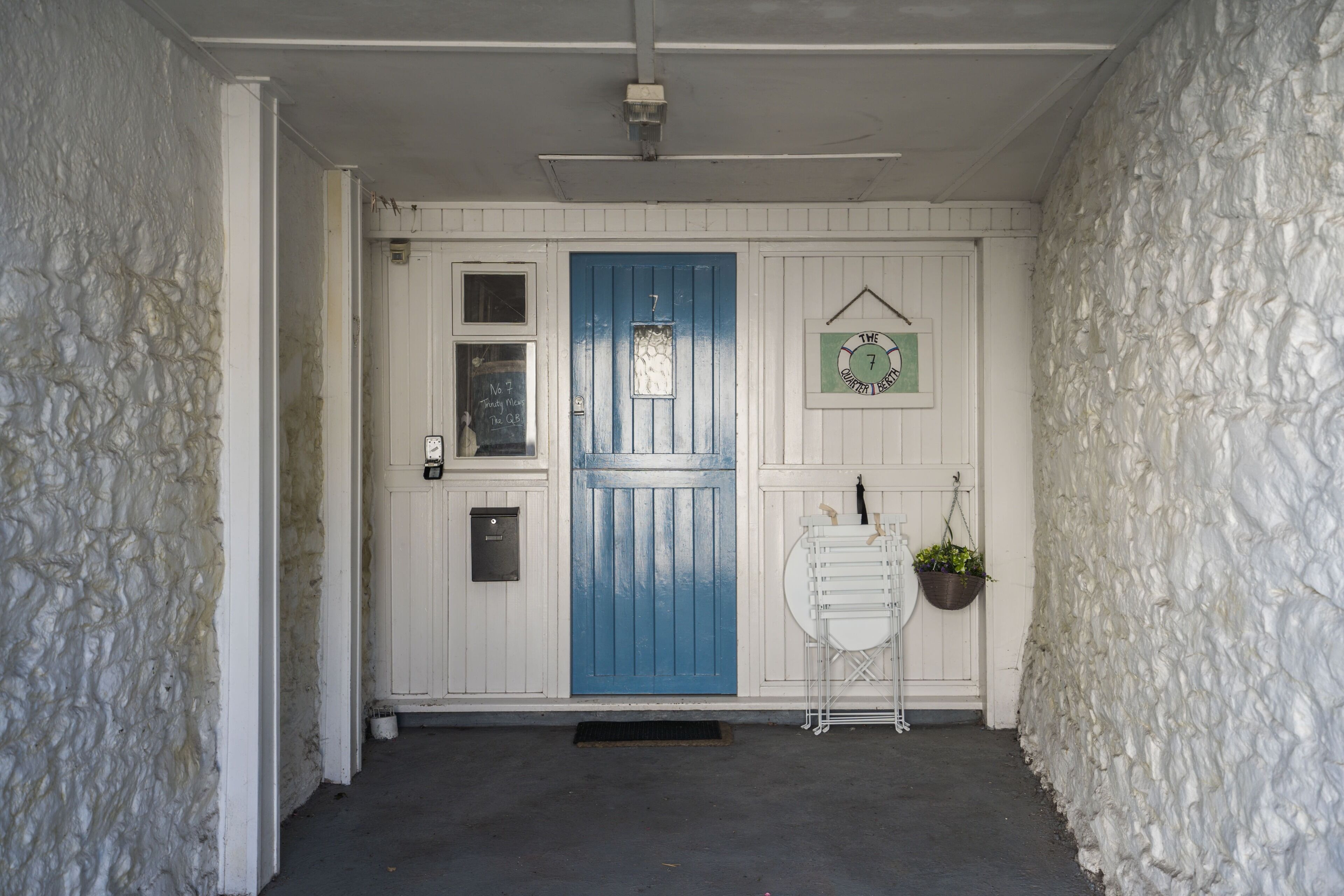Un edificio blanco con una puerta azul, una ventana pequeña y un letrero sobre la puerta.