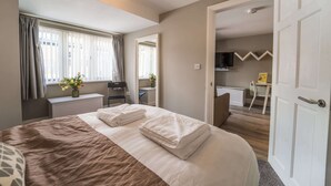 Een netjes ingerichte slaapkamer met een groot bed, een bureau en een televisie in de aangrenzende kamer.