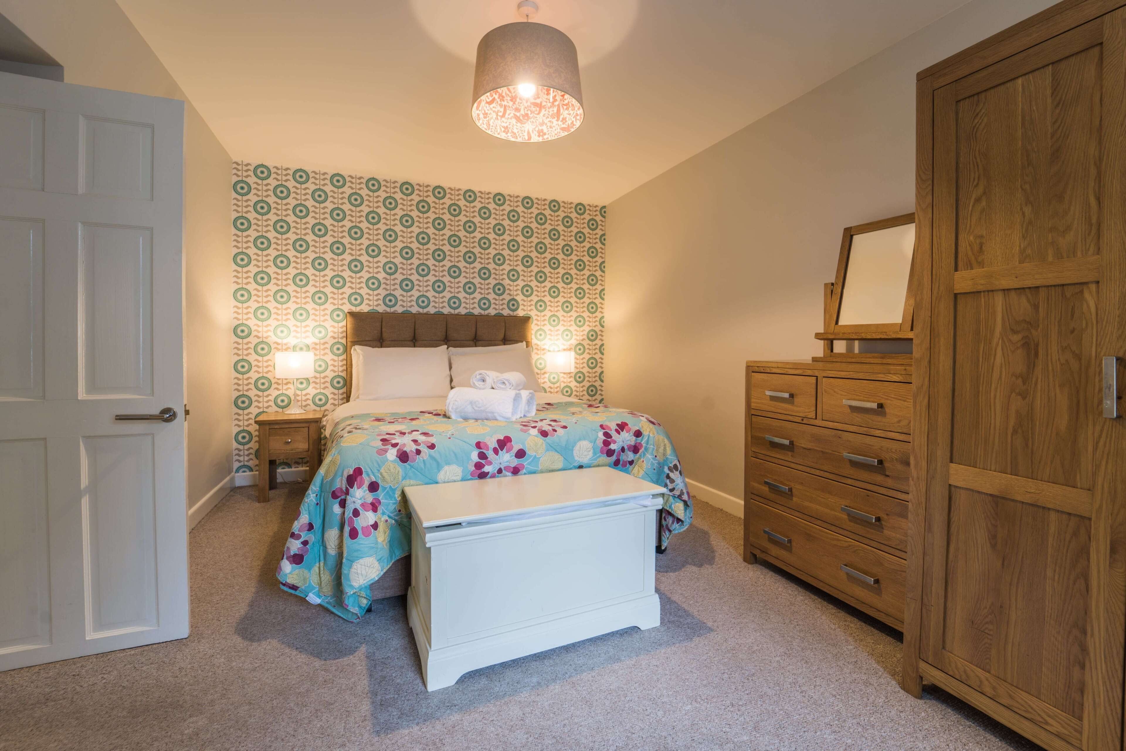 A bedroom with a bed, bedside tables, a wooden wardrobe, and a patterned wallpaper.
