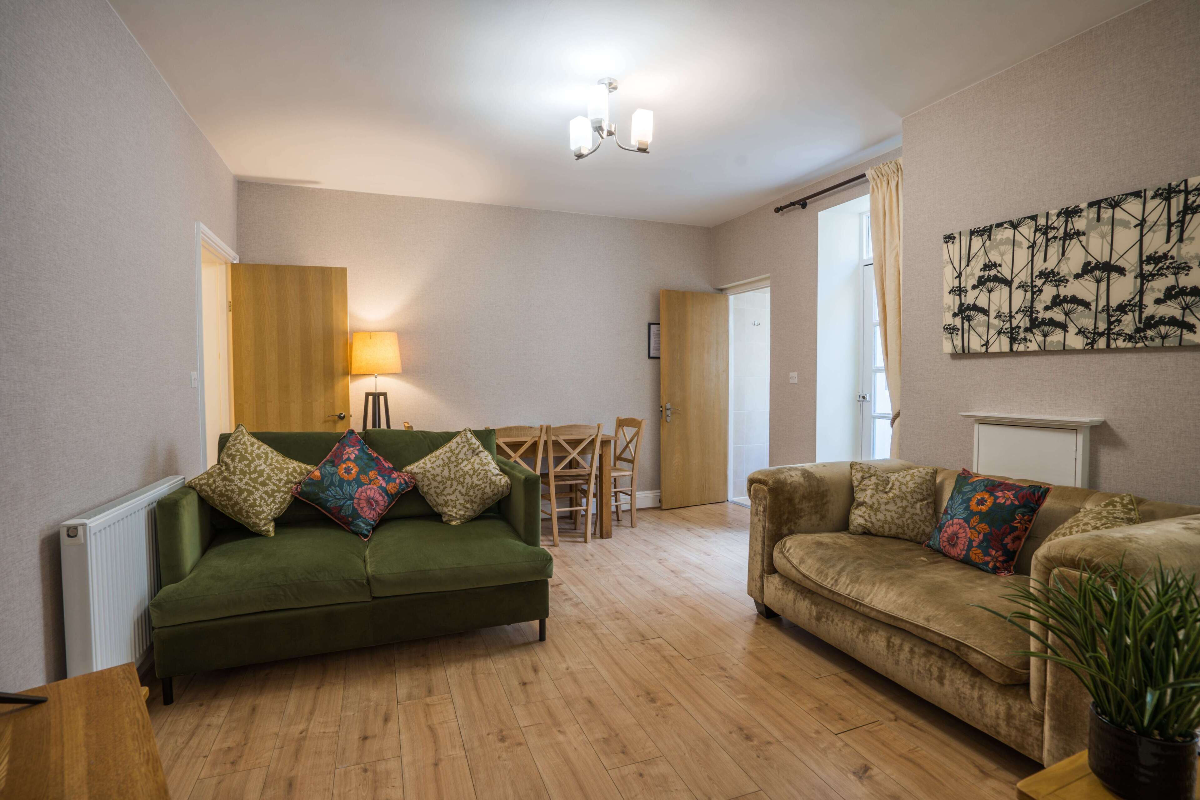 A living room with two sofas, a wooden floor, a dining table, and a lamp.