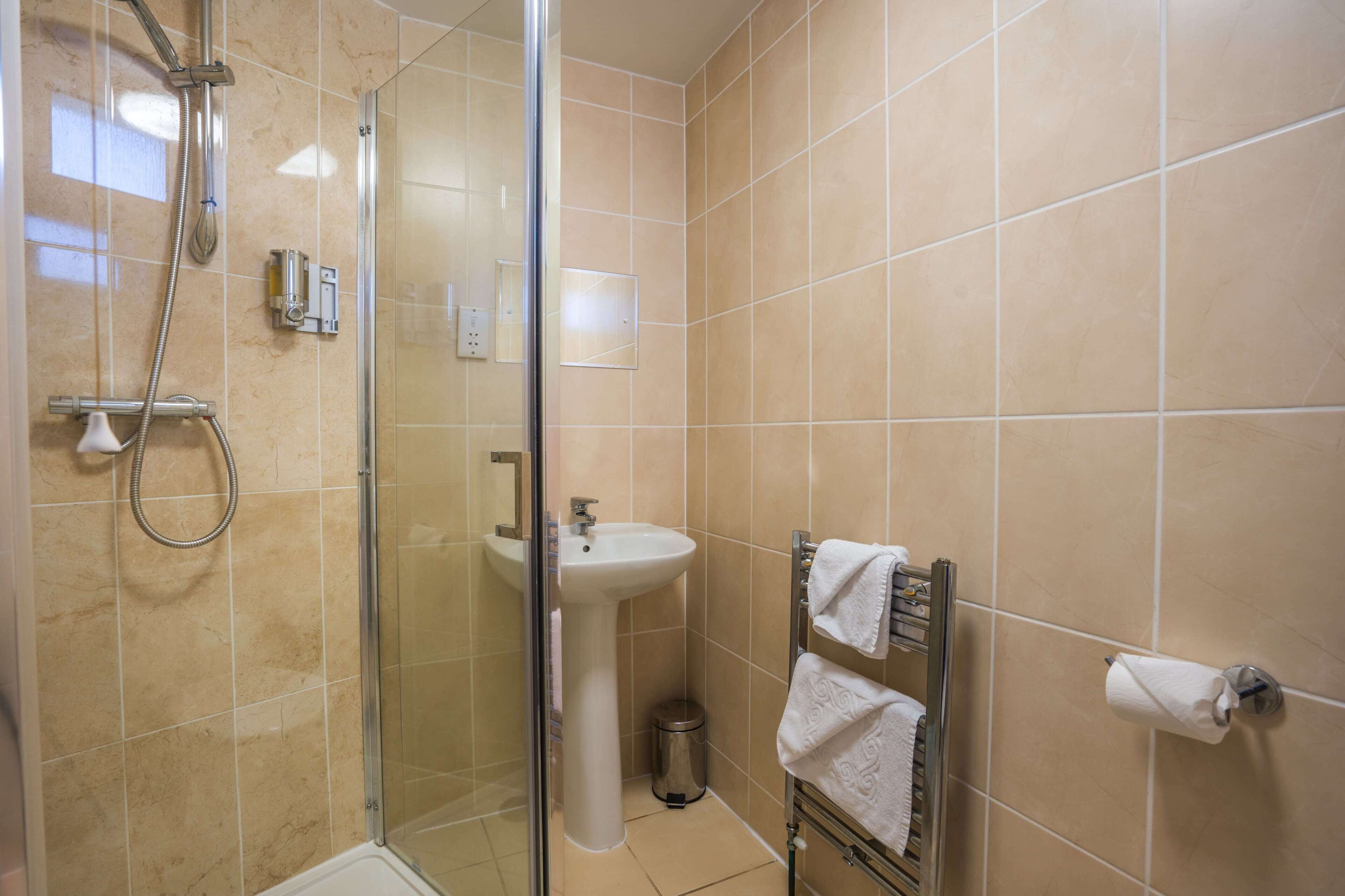 Ein Badezimmer mit Duschkabine, Waschbecken und Handtuchhalter mit Handtüchern.