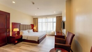 Ein Hotelzimmer mit einem großen Bett, einem Schreibtisch mit Lampe, einem Sessel und einem Fernseher.