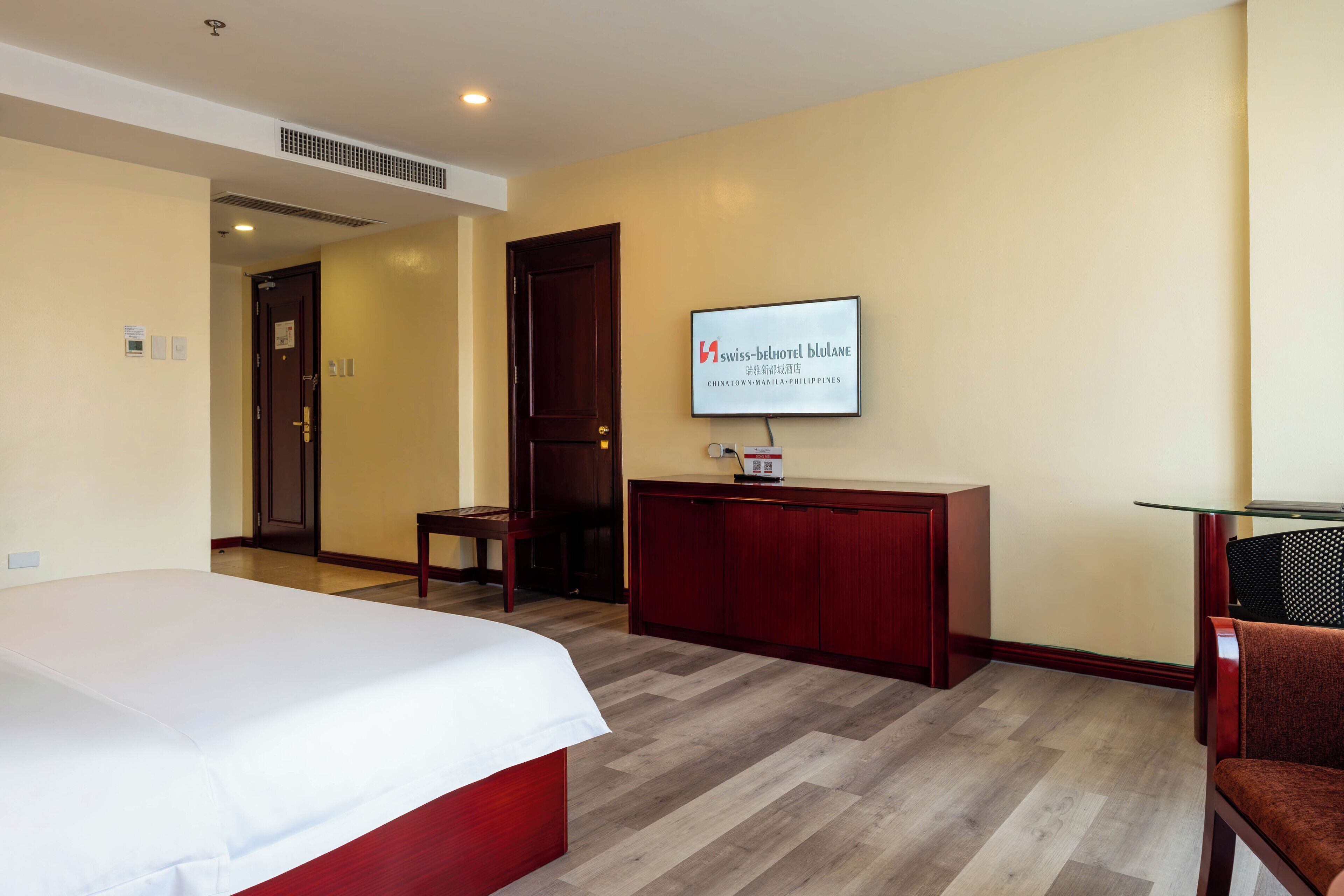 A hotel room with a bed, a desk, a chair, and a television displaying the hotel name.