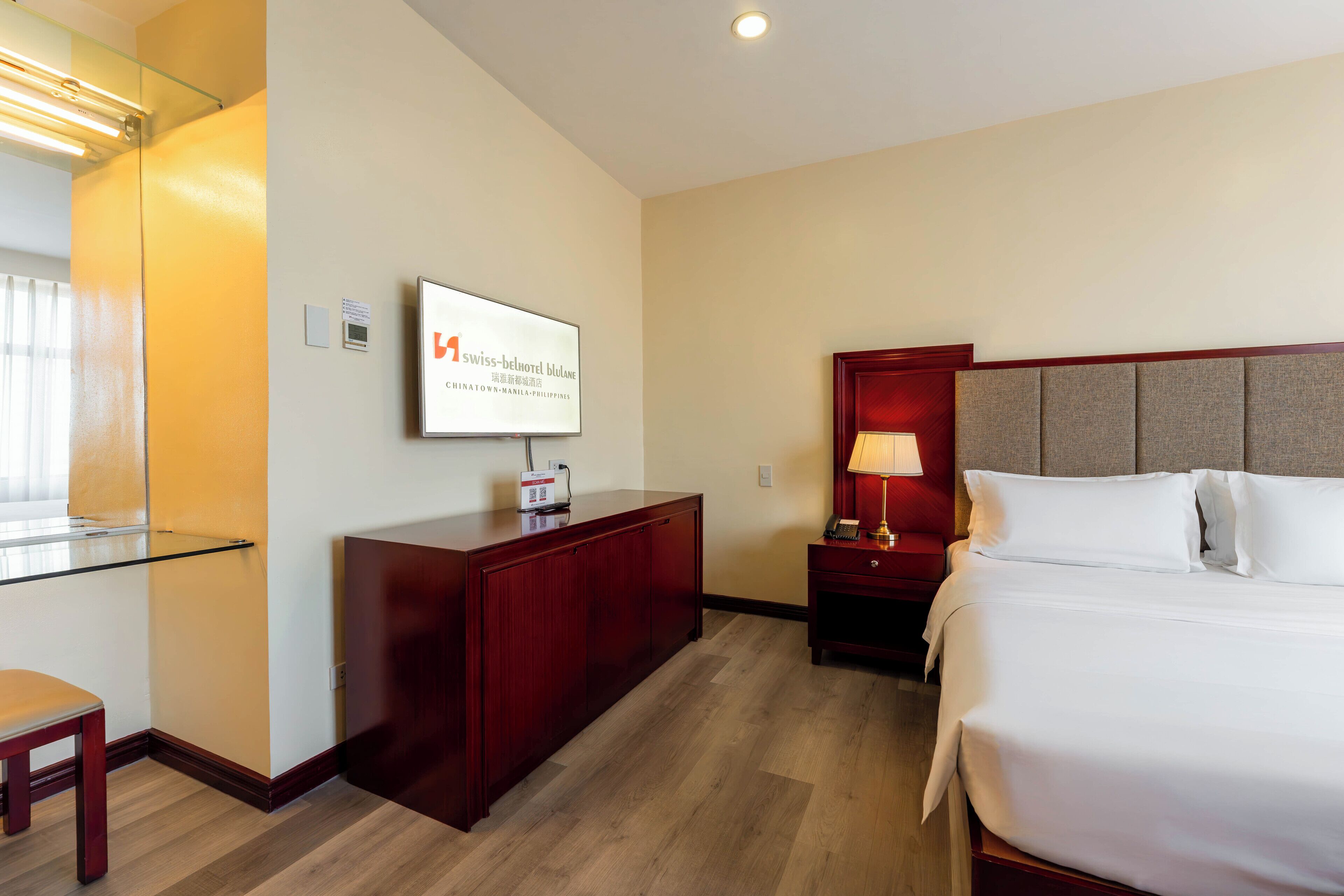 A hotel room with a bed, a desk, a chair, a TV, and a nightstand.