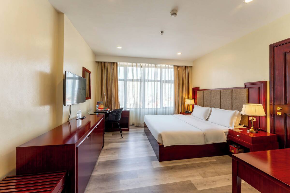 A hotel room with a bed, desk, chair, TV, and a window with curtains.