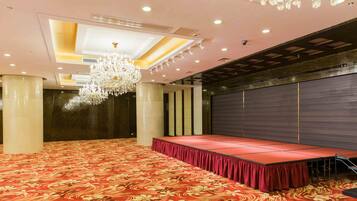A large conference room with a red carpet, a stage with a red backdrop, and a chandelier.