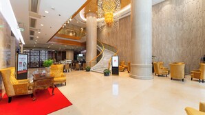 Eine großzügige Lobby mit einer imposanten Treppe, bequemen Sitzgelegenheiten und einem modernen Kronleuchter.