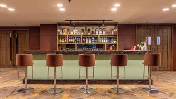 A bar area with a marble countertop, multiple stools, and a shelf with various bottles and glasses.