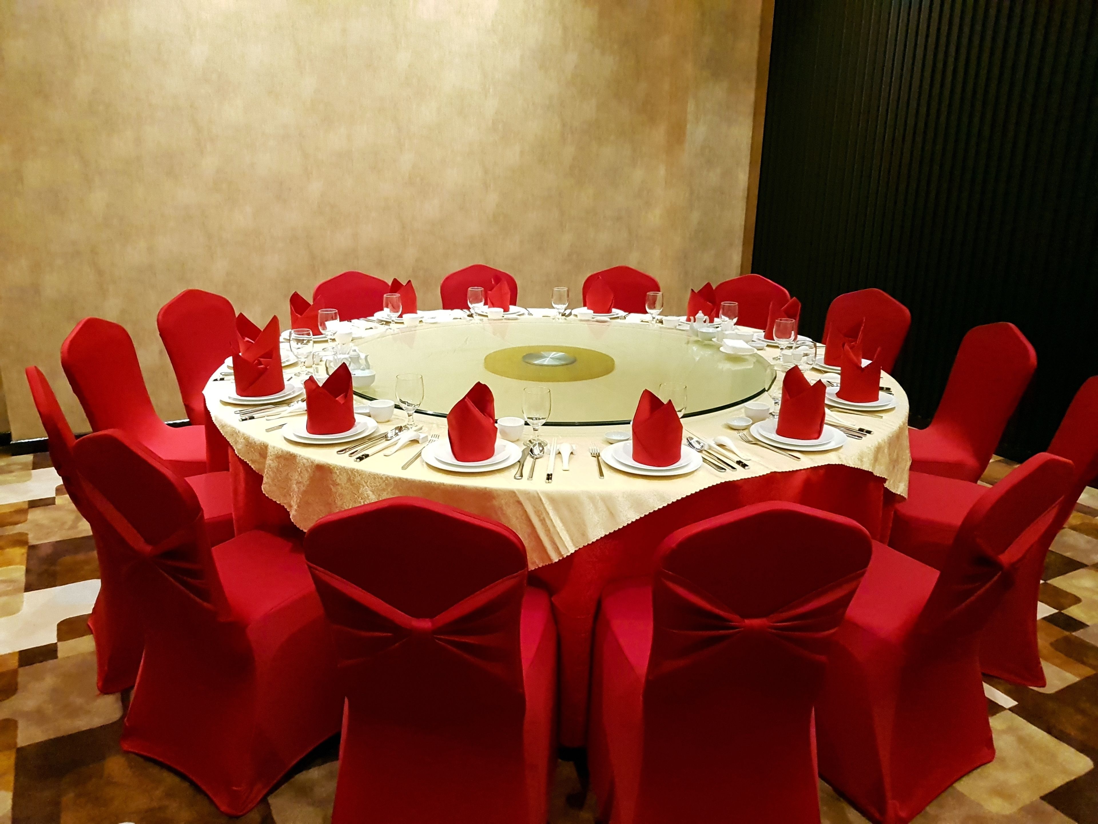 A round table with red chairs, white tablecloth, and red napkins.