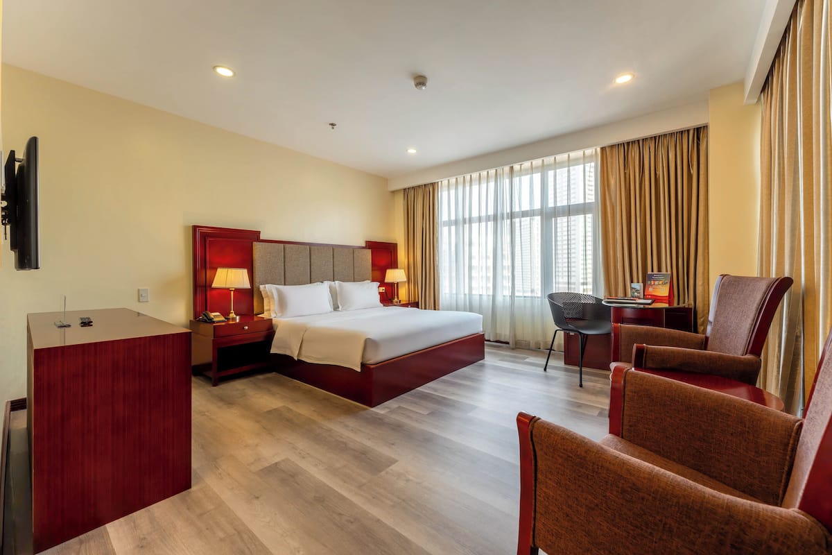 A hotel room with a bed, desk, and two armchairs.