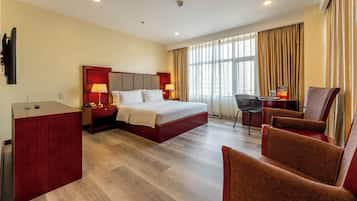 A hotel room with a bed, desk, and two armchairs.