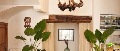 A rustic interior with exposed wooden beams, a chandelier, potted plants, and a fireplace.