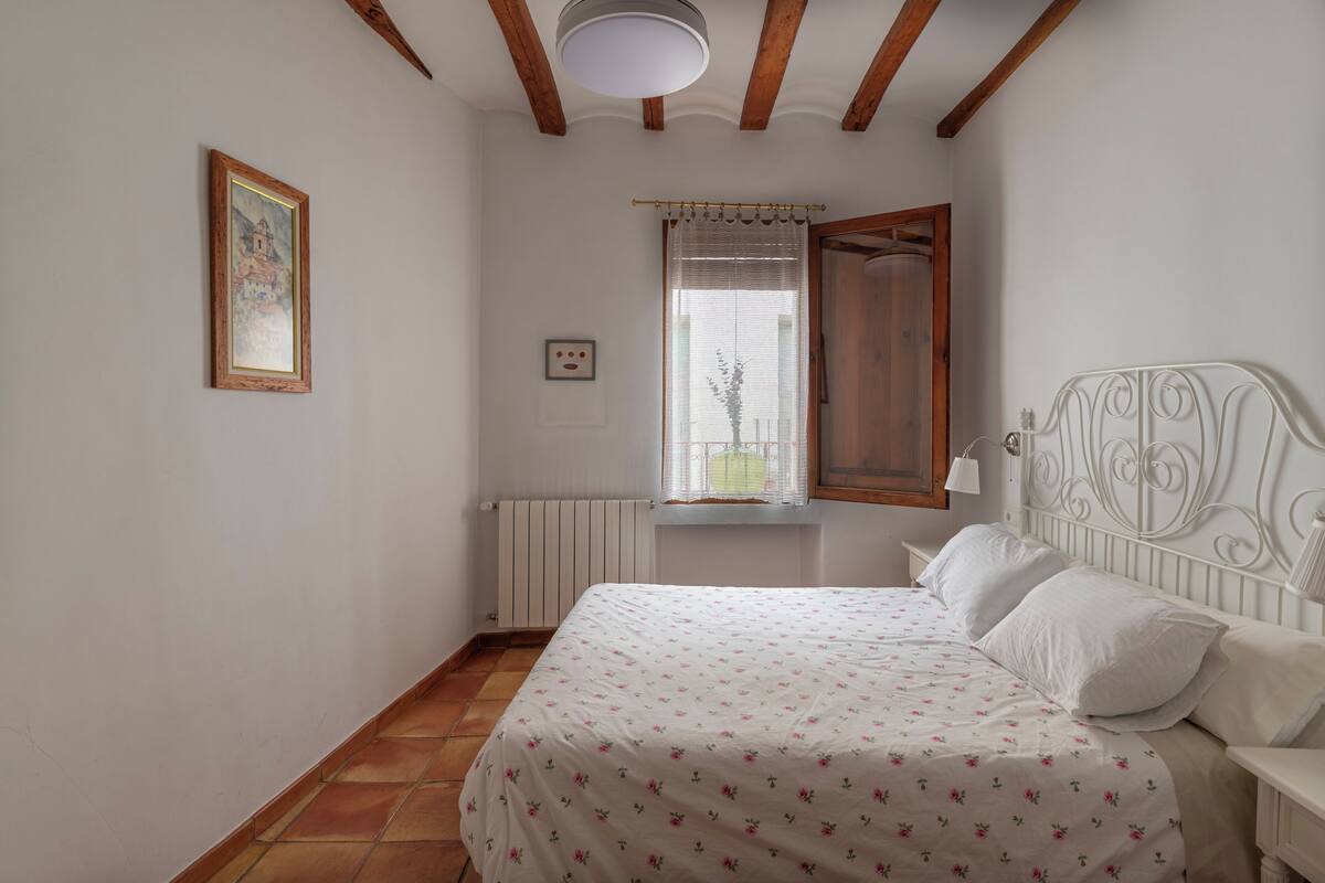 A bedroom with a bed, a window with curtains, a radiator, and a picture on the wall.
