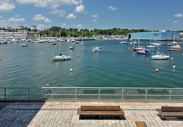 A marina with boats, a waterfront promenade, and buildings in the background.