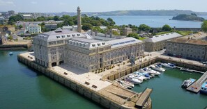 Ein großes, historisches Gebäude mit einem markanten Turm, gelegen an einer Marina mit mehreren angestaubten Booten.
