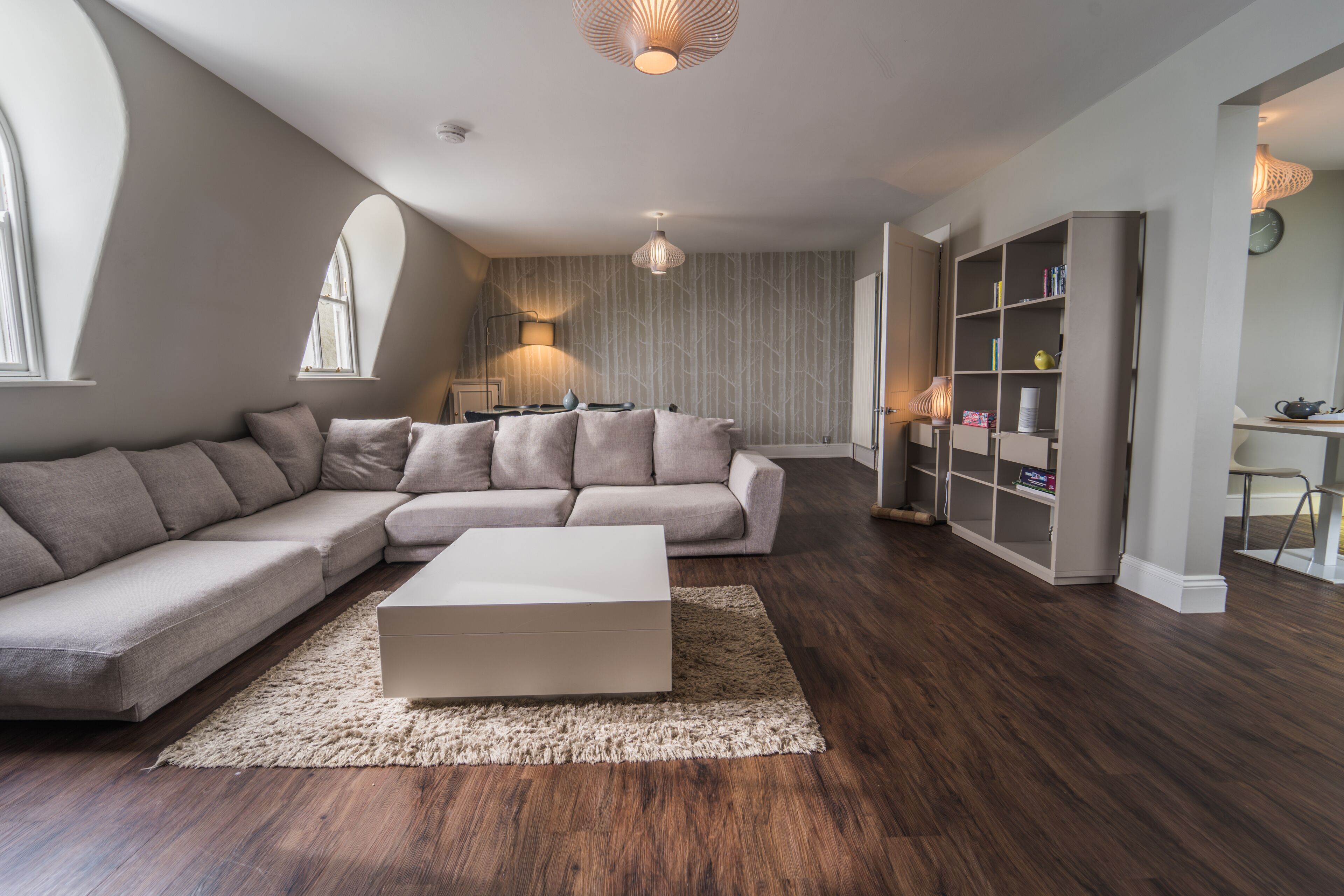A modern living room with a sectional sofa, a white coffee table, and a bookshelf.