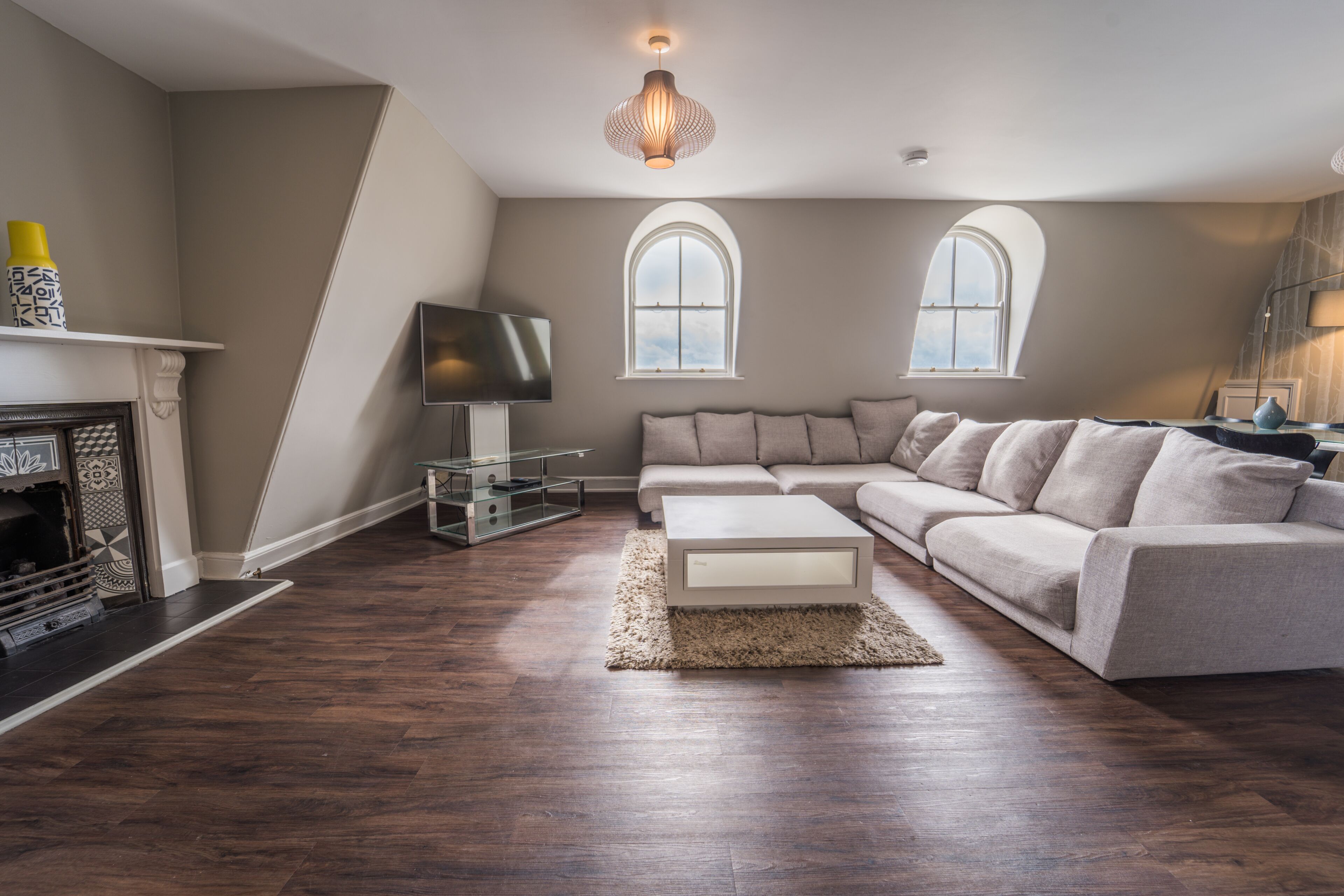 A living room with a sectional sofa, a flat-screen TV, a fireplace, and two arched windows.