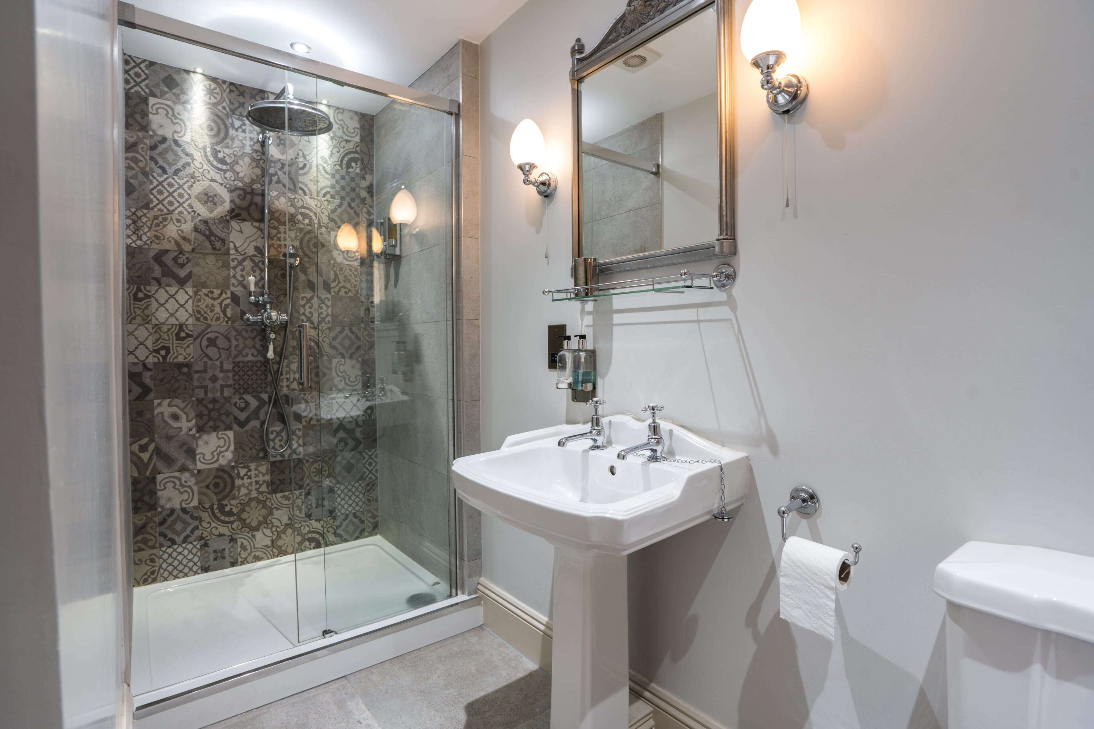 Een moderne badkamer met een douchecabine van glas, een wit wastafeltje en een toilet.